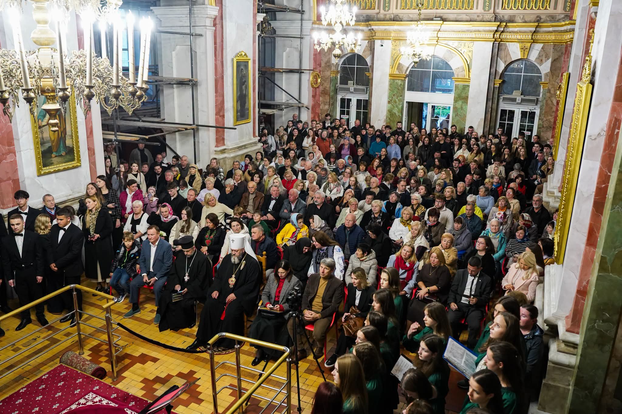 Повний собор слухачів, вигляд згори; у першому ряду архієрей у білому клобуку і священник; праворуч хористки в зелених сукнях
