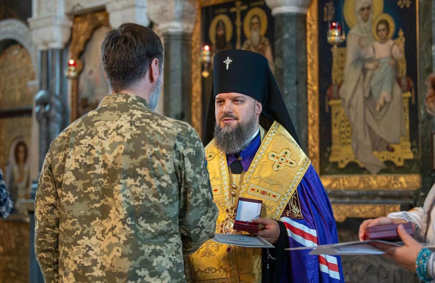Архієпископ Агапіт у святительському облаченні вручає відзнаку військовому в пікселі на тлі іконостаса