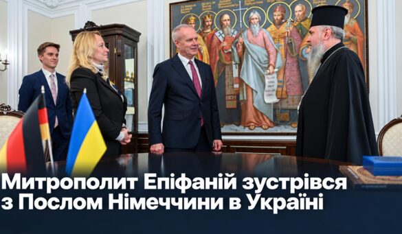 Митрополит Епіфаній у чорному клобуку вітає Посла Німеччини Бориса Руґе та співробітників Посольства; на столі прапорці Німеччини й України, позаду картина зі святими; напис «Митрополит Епіфаній зустрівся з Послом Німеччини в Україні»